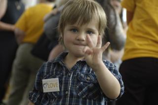 A young child makes an "okay" sign with his hand.