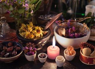 An altar with a lit candle, crowded by jars of herbs and flowers and other ritual objects