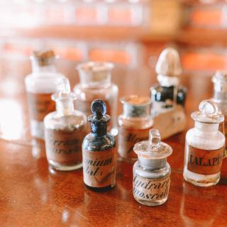 On a wooden surface, tiny antique bottles -- as if herbs or chemicals -- with labels in calligraphy.
