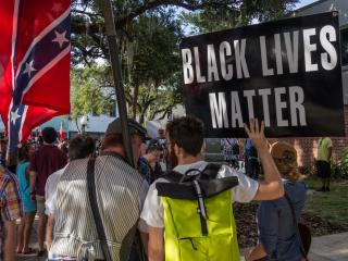 Behind a crowd of protesters, one man holds a Confederate flag while anothr holds a "Black Lives Matter" sign