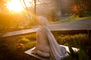 Sunlight shines on a statue of a meditating person..