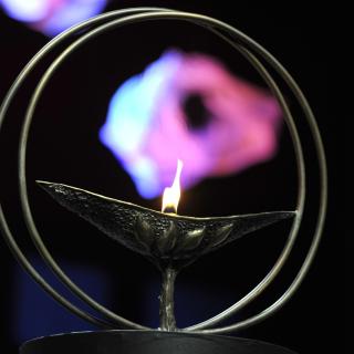 Bronze UUA chalice with flame and multicolored light reflected in background