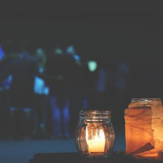 In the foreground, a trio of candles in small jars. In the background, a group of people form a friendly huddle.
