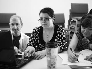 Three people at a table with a coffee cup and a laptop computer.