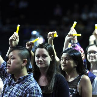 Young adults, of different styles and races, stands in a line holding up glo-sticks.