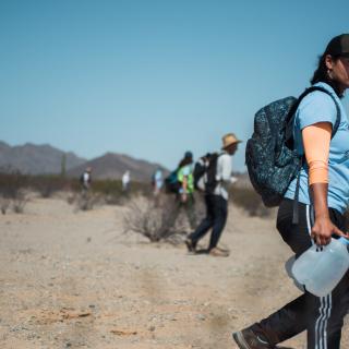 people walking in desert carrying jugs of water