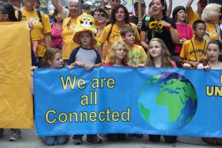 UUs of all ages stand behind a banner with a picture of the earth, reading "We are all connected."