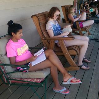 three young adults sit in chairs reading books on a porch
